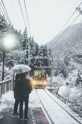 Rear view of man and woman standing at railroad station during snowfall - CAVF55636