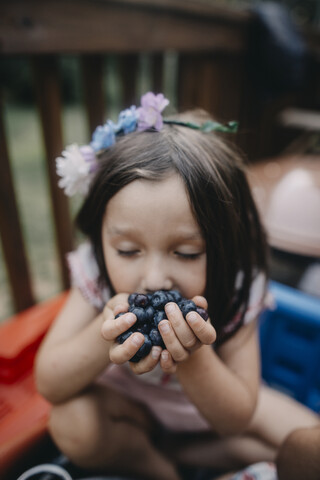 Mädchen mit geschlossenen Augen isst Blaubeeren auf der Veranda, lizenzfreies Stockfoto