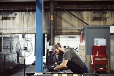 Side view of blue collar worker using hammer and chisel in steel factory - CAVF55670