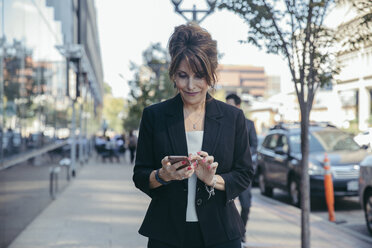 Businesswoman using smart phone on footpath - CAVF55685