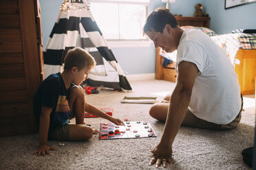 Vater und Sohn spielen Dame, während sie zu Hause auf dem Teppich sitzen - CAVF55686