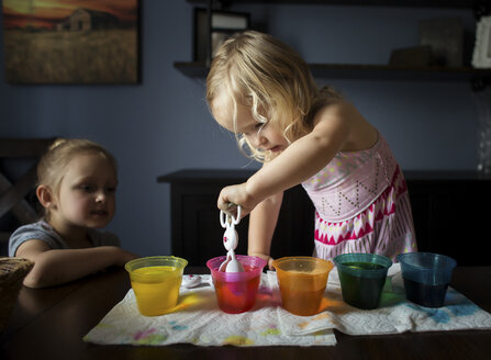 Mädchen betrachtet ihre Schwester bei der Vorbereitung von Ostereiern auf dem Tisch zu Hause - CAVF55687