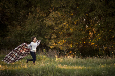 Verspieltes Mädchen hält Picknickdecke beim Laufen im Park - CAVF55699