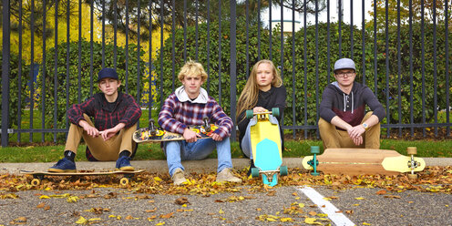 Porträt von Freunden mit Skateboards, die im Herbst auf einem Fußweg im Park sitzen - CAVF55710