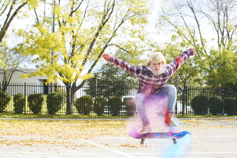Porträt eines Mannes mit Puderfarbe, der beim Skateboardfahren in einem Park im Herbst springt, lizenzfreies Stockfoto