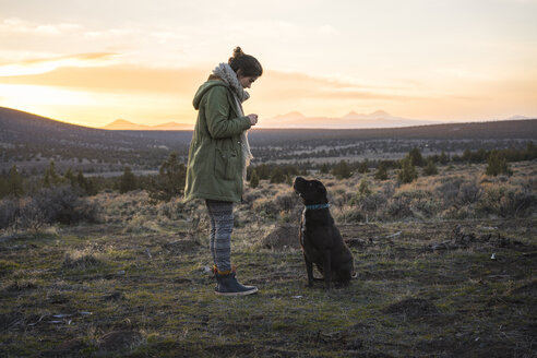 Seitenansicht einer Frau, die mit ihrem Hund auf einem Feld steht, gegen den Himmel bei Sonnenuntergang - CAVF55755