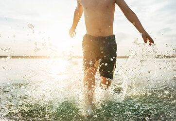 Midsection von shirtless Junge zu Fuß im Meer am Strand während des sonnigen Tages - CAVF55757