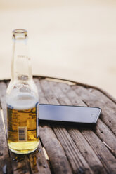 High angle view of mobile phone and beer bottle on table at beach - CAVF55771