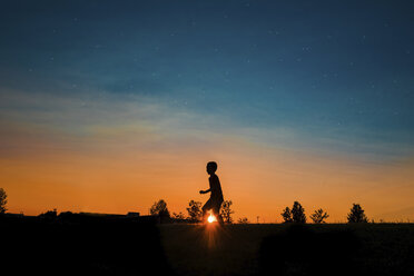 Silhouette eines Jungen, der bei Sonnenuntergang auf einem Feld gegen den Himmel läuft - CAVF55801