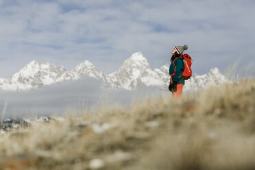 Side view of female hiker with backpack standing against snowcapped mountains and cloudy sky - CAVF55828