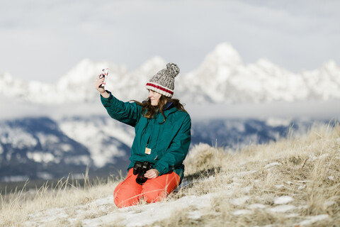 Female hiker taking selfie with smart phone against mountains during winter stock photo
