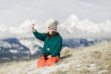 Weiblicher Wanderer nimmt Selfie mit Smartphone gegen Berge im Winter - CAVF55833