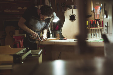 Handwerker schnitzt Holz, während er eine Gitarre auf einer Werkbank in einer Werkstatt herstellt - CAVF55843