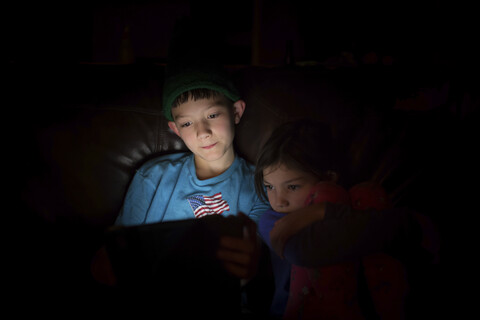 Geschwister benutzen einen Tablet-Computer, während sie in der Dunkelkammer zu Hause sitzen, lizenzfreies Stockfoto