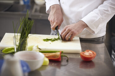 Nahaufnahme eines Kochs, der Gemüse auf einem Schneidebrett in einer Großküche hackt - CAVF55853