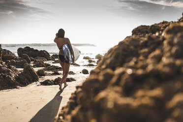 Frankreich, Bretagne, junge Frau mit Surfbrett an einem felsigen Strand am Meer - UUF15883