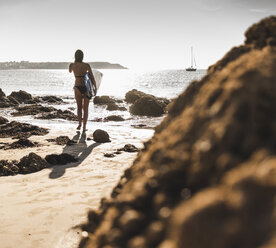 Frankreich, Bretagne, junge Frau mit Surfbrett an einem felsigen Strand am Meer - UUF15885