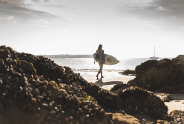 Frankreich, Bretagne, junge Frau mit Surfbrett an einem felsigen Strand am Meer - UUF15888