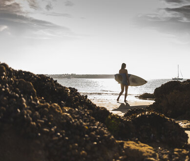 Frankreich, Bretagne, junge Frau mit Surfbrett an einem felsigen Strand am Meer - UUF15889