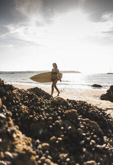 Frankreich, Bretagne, junge Frau mit Surfbrett an einem felsigen Strand am Meer - UUF15891