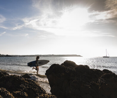 Frankreich, Bretagne, junge Frau mit Surfbrett läuft im Meer - UUF15894