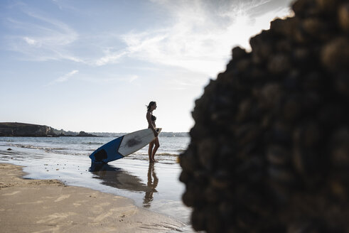 Frankreich, Bretagne, junge Frau mit Surfbrett am Meer stehend - UUF15895