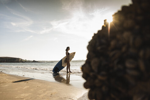 Frankreich, Bretagne, junge Frau mit Surfbrett am Meer stehend - UUF15896