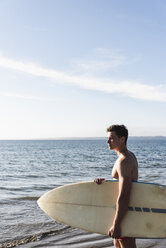 Frankreich, Bretagne, junger Mann mit Surfbrett am Meer stehend - UUF15898