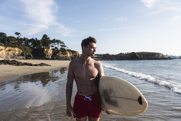 Frankreich, Bretagne, junger Mann mit Surfbrett am Meer stehend - UUF15900