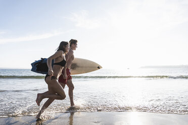 Frankreich, Bretagne, junges Paar mit Surfbrett läuft im Meer - UUF15902