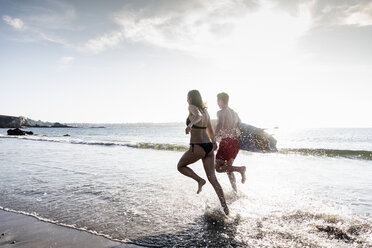 France, Brittany, young couple with surfboard running in the sea - UUF15903