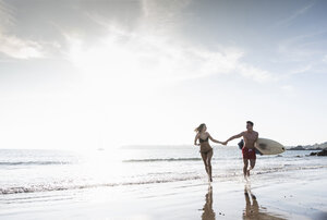 Frankreich, Bretagne, glückliches junges Paar mit Surfbrett läuft Hand in Hand im Meer - UUF15907