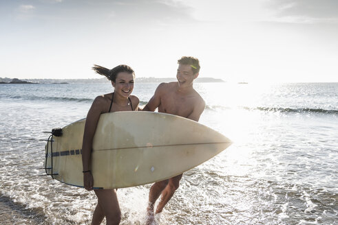 Frankreich, Bretagne, glückliches junges Paar mit Surfbrett läuft im Meer - UUF15910