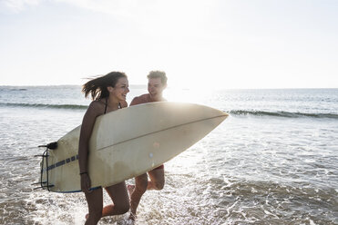 Frankreich, Bretagne, glückliches junges Paar mit Surfbrett läuft im Meer - UUF15911