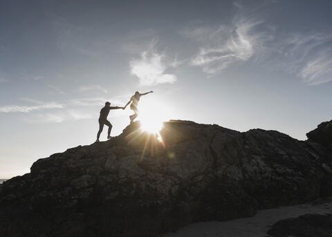 France, Brittany, young couple climbing on a rock at sunset stock photo