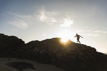 Frankreich, Bretagne, junger Mann läuft bei Sonnenuntergang auf einem Felsen - UUF15938