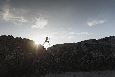 Frankreich, Bretagne, junger Mann springt bei Sonnenuntergang auf einen Felsen - UUF15939