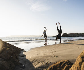 Frankreich, Bretagne, junger Mann, der neben seiner Freundin am Strand einen Handstand macht - UUF15946