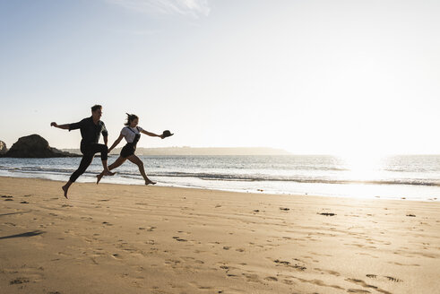 Frankreich, Bretagne, glückliches junges Paar springt bei Sonnenuntergang am Strand - UUF15949