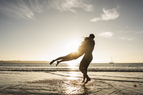 Frankreich, Bretagne, glückliches junges Paar, das sich bei Sonnenuntergang am Strand umarmt - UUF15952
