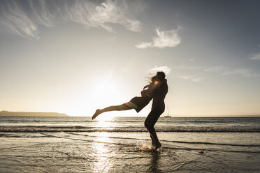 France, Brittany, happy young couple hugging on the beach at sunset - UUF15953