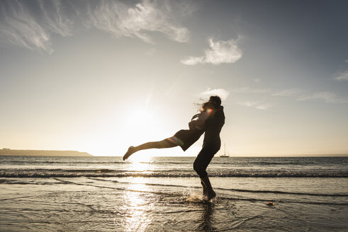 Frankreich, Bretagne, glückliches junges Paar, das sich bei Sonnenuntergang am Strand umarmt - UUF15953