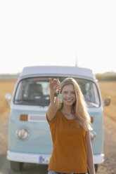 Glückliche junge Frau mit Autoschlüssel am Wohnmobil in ländlicher Landschaft - GUSF01387