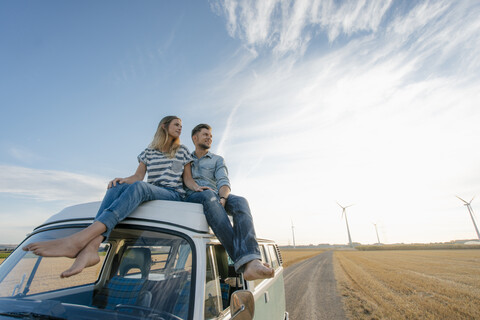 Ehepaar sitzt auf einem Wohnmobil in ländlicher Landschaft mit Windrädern im Hintergrund, lizenzfreies Stockfoto