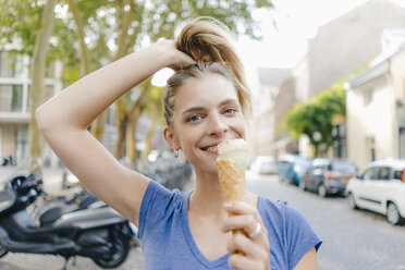 Netherlands, Maastricht, portrait of happy blond young woman holding ice cream cone in the city - GUSF01398