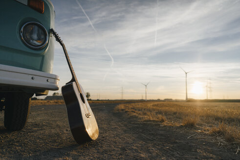 Gitarre lehnt an Wohnmobil in ländlicher Landschaft mit Windrädern bei Sonnenuntergang - GUSF01404