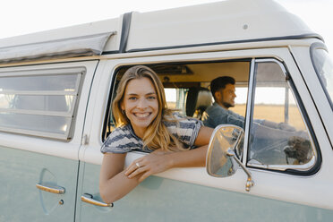 Porträt einer glücklichen Frau, die sich aus dem Fenster eines Wohnmobils lehnt, in dem ein Mann fährt - GUSF01412
