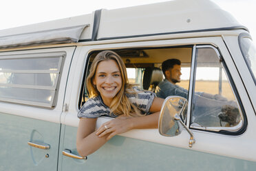 Portrait of happy woman leaning out of window of a camper van with man driving - GUSF01412