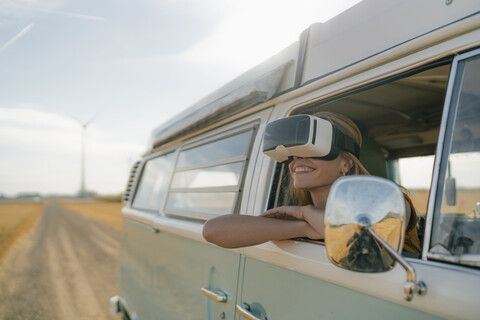 Smiling woman wearing VR glasses leaning out of window of a camper van stock photo