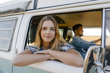 Portrait of smiling woman leaning out of window of a camper van with man driving - GUSF01421